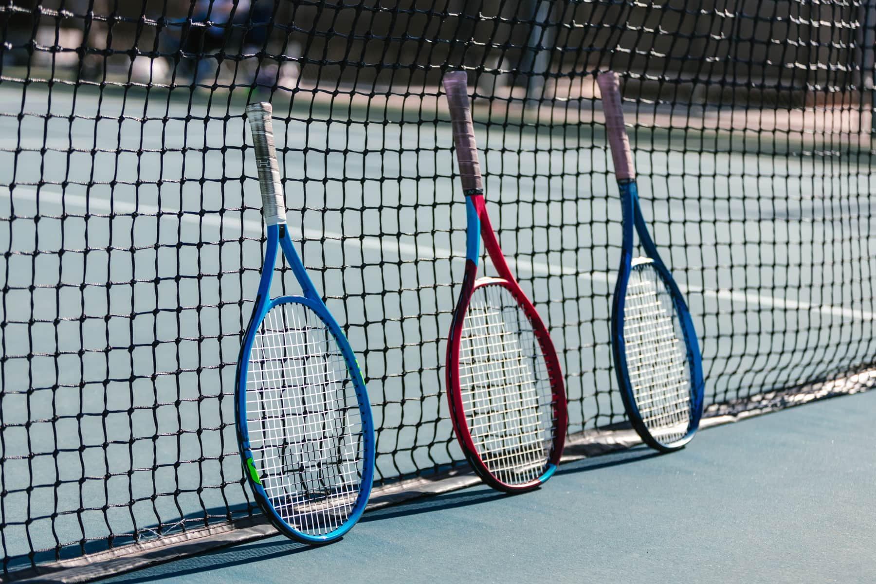 Tennis rackets lined against the fence of an outdoor hard court