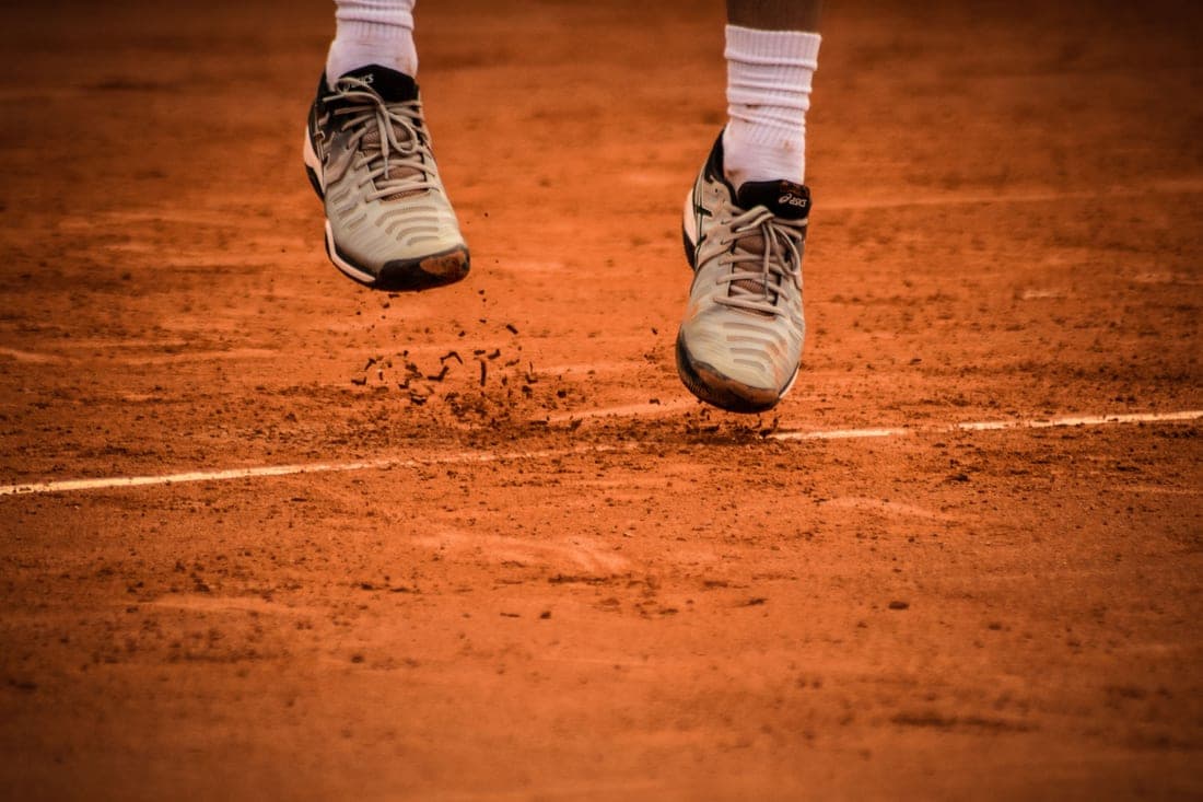 Pair of tennis shoes on a clay court with herringbone tread visible