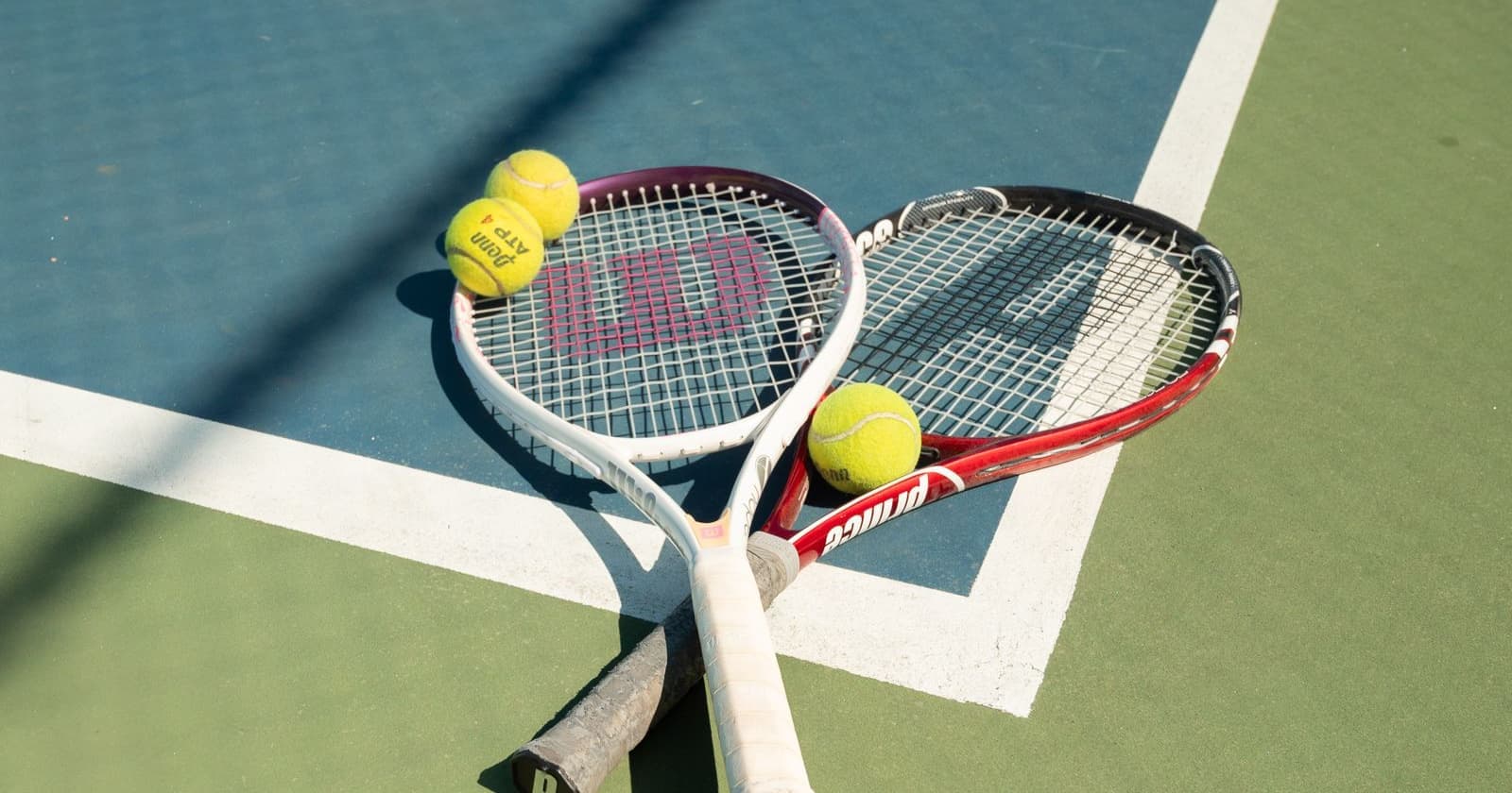 Two tennis rackets laid side by side on a sunlit outdoor court