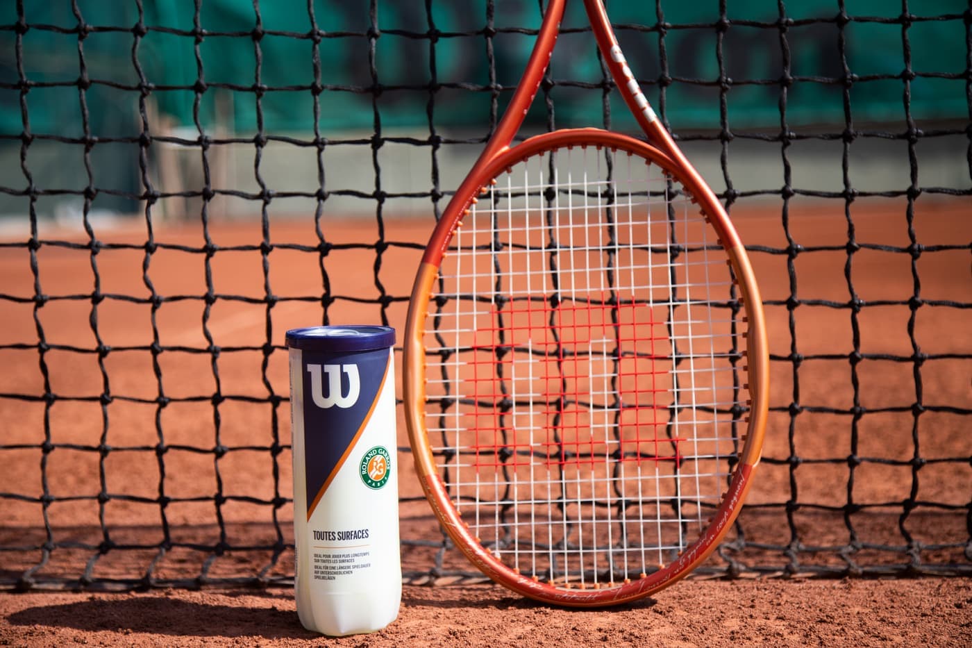 A can of tennis balls open beside loose balls on a hard court