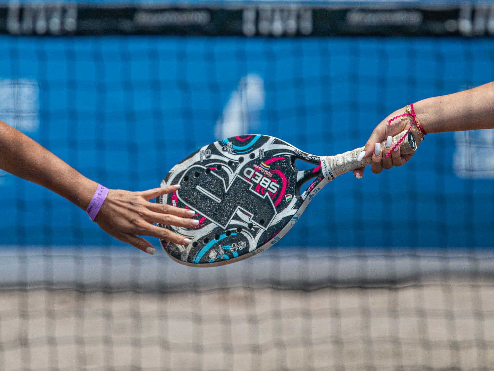 A padel racket held in one hand on an enclosed court