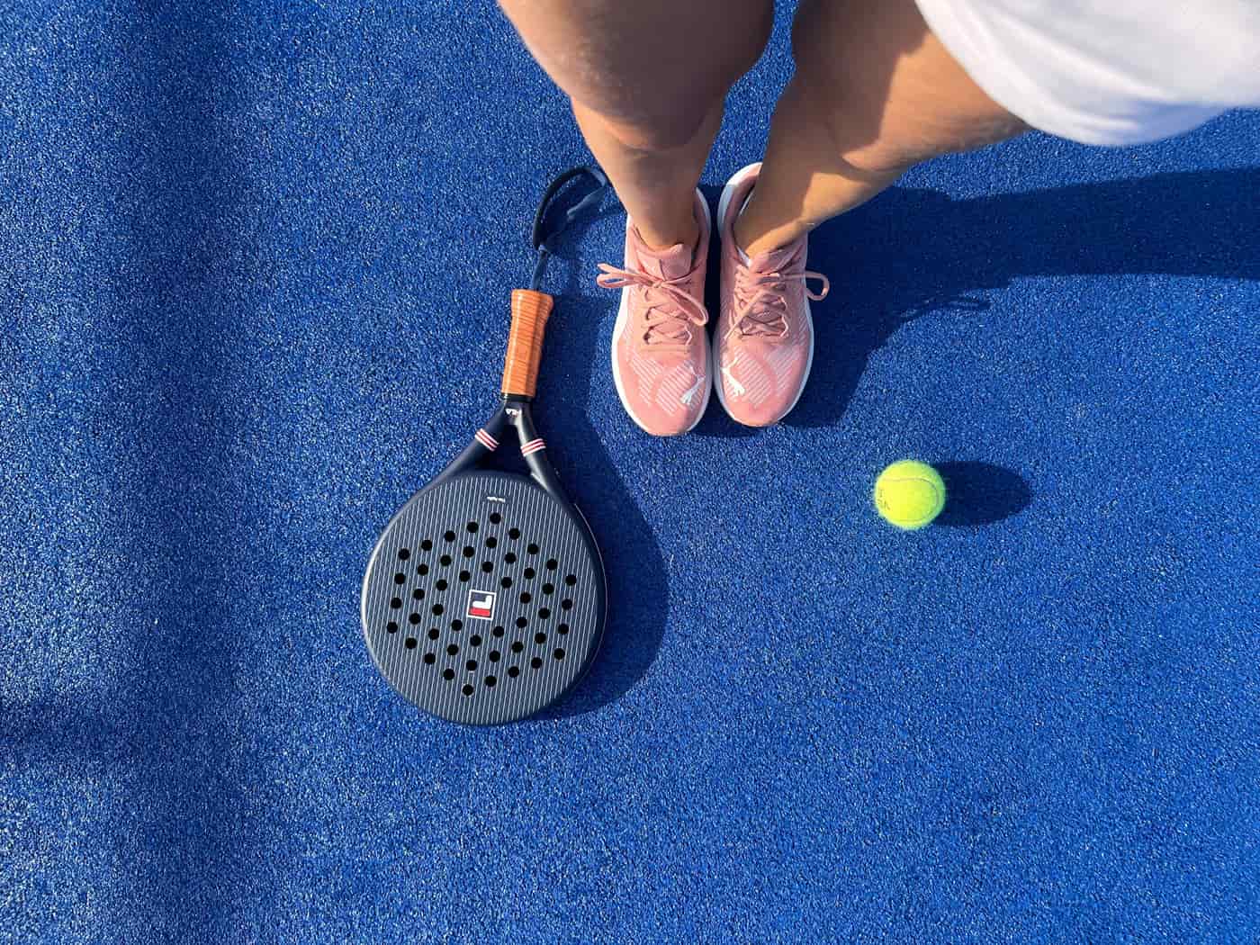 A padel racket held up on an enclosed padel court