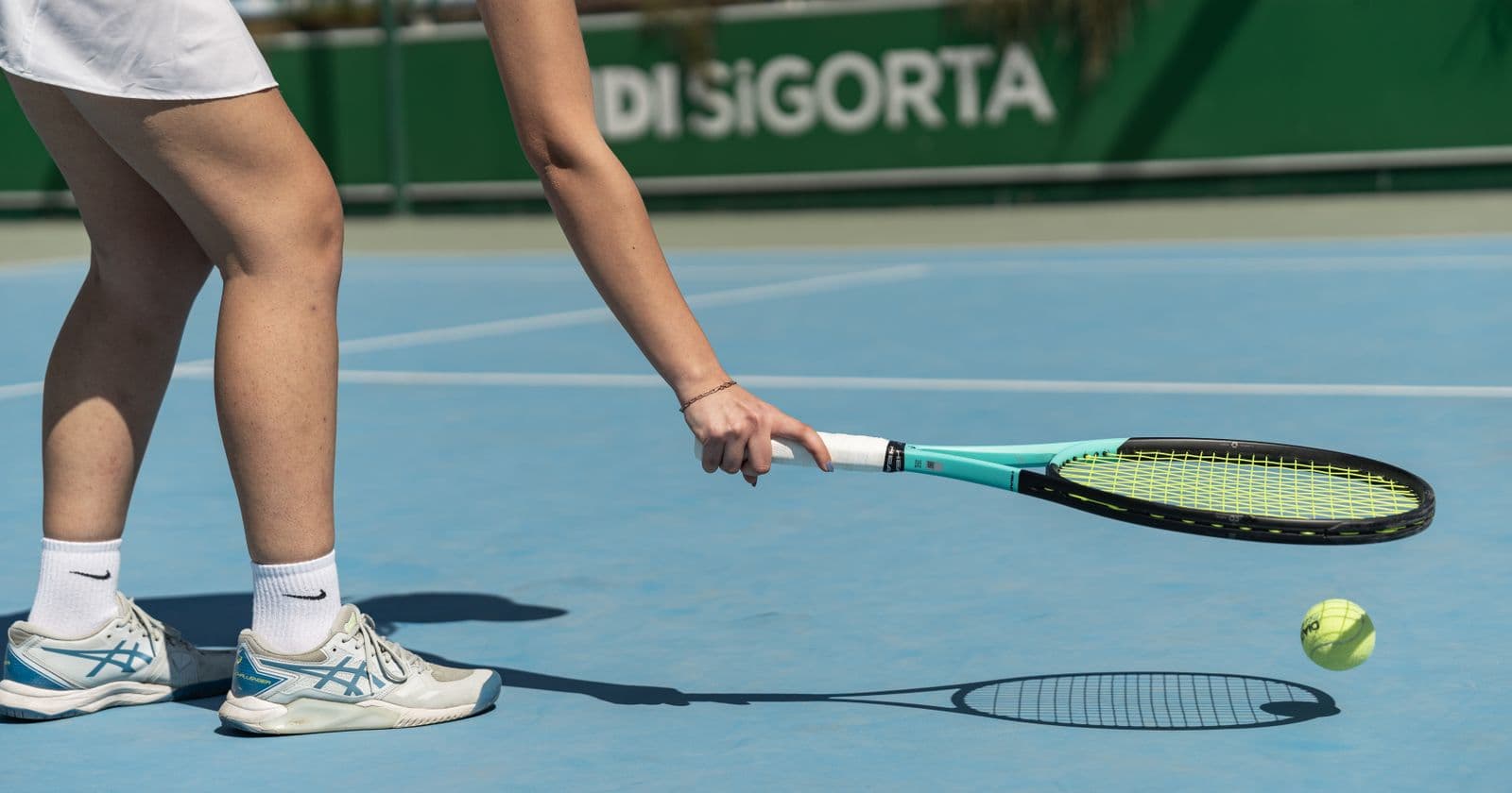 A woman's legs and court shoes mid-stride on an outdoor hard court